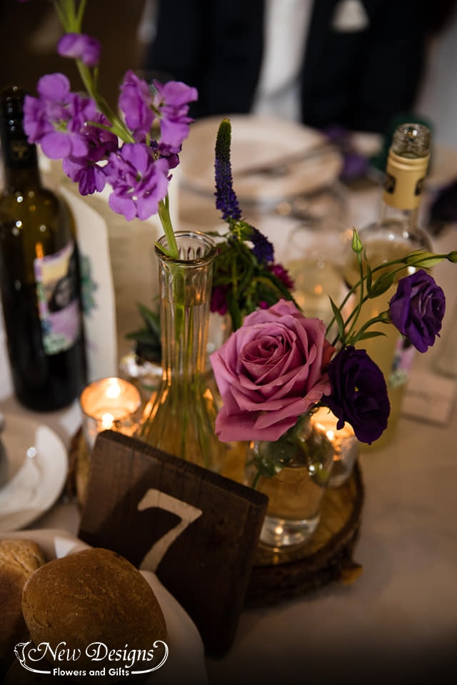 A lovely centerpiece of various heights and shapes of glass vases, featuring purple and green flowers and succulents of various shades heights and textures.